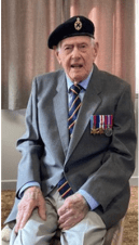 Image of REME Gold Beach Veteran Dennis Tocknell in medals sat on a chair.